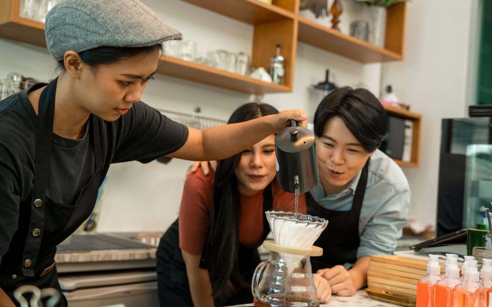 barista-pouring-boiling-water-from-kettle-to-drip-coffee-maker-at-the-bar-of-the-modern-cafe-e1651630662286